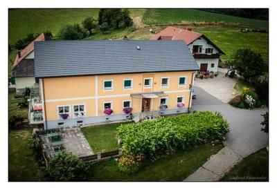 Ein Luftbild eines gelben Hauses mit grauem Dach, umgeben von üppigem Grün, einer Auffahrt und einem Nachbarhaus mit rotem Dach.