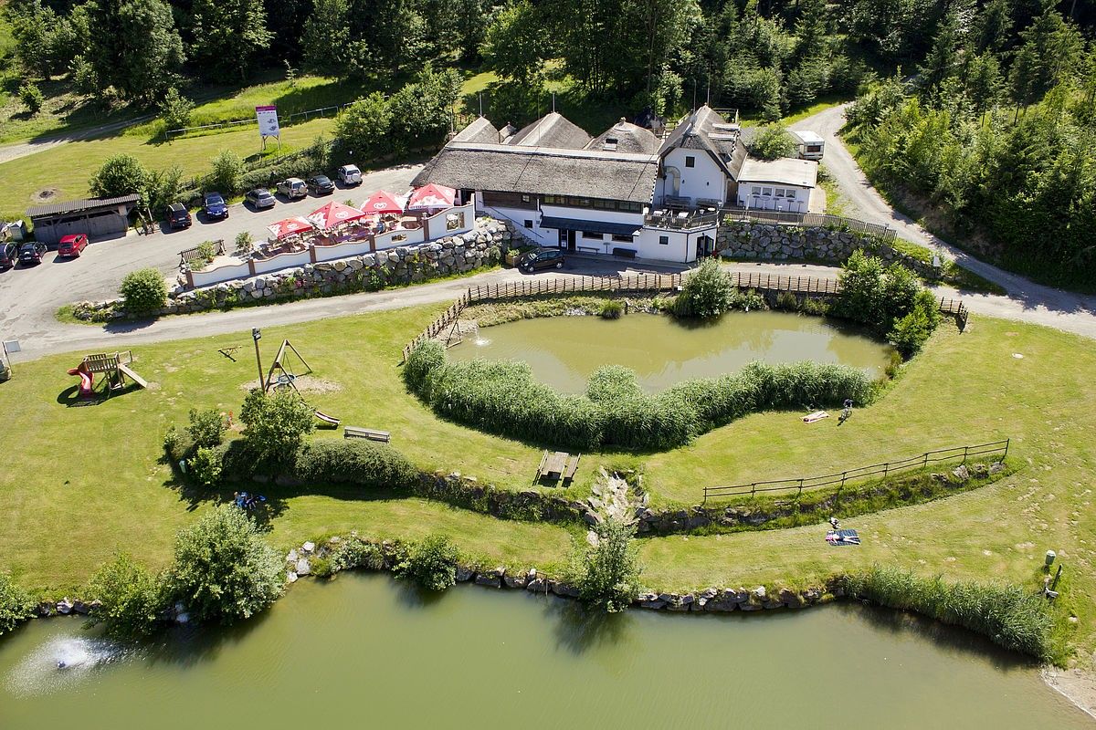Ein Blick von oben auf ein Resort mit einem großen Teich, einem Spielbereich und einem Gebäude mit Strohdach. Autos sind an der Seite geparkt.