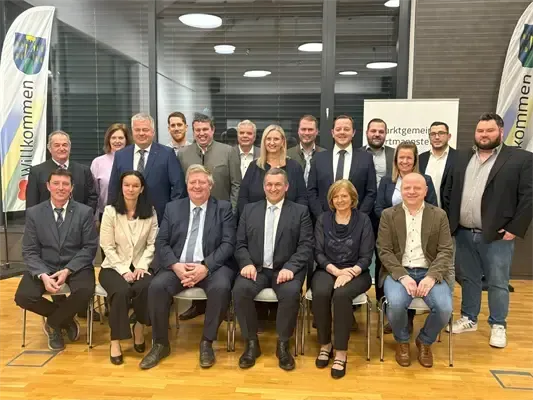 Eine Gruppe von Männern und Frauen in Geschäftskleidung sitzt auf Stühlen und posiert für ein Foto in einem modernen Bürogebäude.