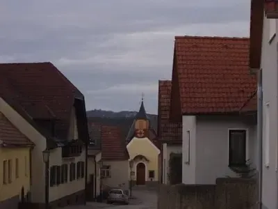 Eine enge Straße mit einer kleinen Kirche in der Mitte, umgeben von Gebäuden mit roten Dächern und einem Auto, das davor geparkt ist.