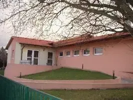 Ein rosafarbenes Haus mit einem roten Dach und mehreren Fenstern, umgeben von einem grünen Rasen und einem grünen Zaun.