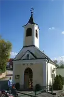 Eine kleine weiße Kirche mit einem Dachreiter und Glockenturm steht unter einem blauen Himmel. Eine Person geht vor der Kirche.