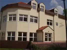 Ein großes beiges Gebäude mit vielen Fenstern, einem roten Dach und einem Schild mit Text und einem Wappen an der Wand.