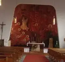 Ein Kircheninneres mit einer großen Wandmalerei hinter dem Altar, die religiöse Figuren zeigt. Der Altar ist mit Kerzen und einem Kreuz geschmückt, und die Kirchenbänke sind symmetrisch auf beiden Seiten angeordnet.