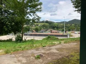 Ein breiter Blick auf eine Sportanlage mit einem Rasenfeld, Bäumen und einem Auto in der Ferne unter einem bewölkten Himmel.