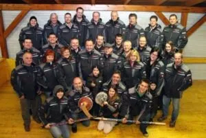 Eine Gruppe von Menschen in gleichen schwarzen Jacken posiert für ein Foto mit Eishockeyschlägern und einem Schild.