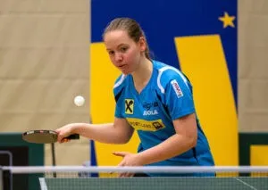 Eine Frau spielt Tischtennis, hält einen Schläger und bereitet sich darauf vor, einen weißen Ball zu schlagen.