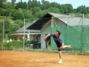Ein junger Mann in Tennisausrüstung befindet sich auf einem Tennisplatz in einer Backhandposition.