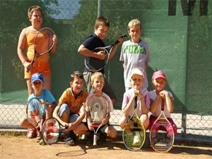 Eine Gruppe von Kindern mit Tennisschlägern posiert für ein Foto vor einem grünen Netz.
