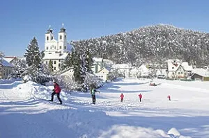 Eine Gruppe von Menschen in Winterkleidung, die in einer verschneiten Landschaft mit einer Kirche im Hintergrund spazieren.