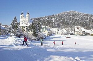 Eine Gruppe von Menschen in Winterkleidung, die in einer verschneiten Landschaft mit einer Kirche im Hintergrund spazieren.