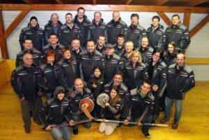 Eine Gruppe von Menschen in gleichen schwarzen Jacken posiert für ein Foto mit Eishockeyschlägern und einem Schild.