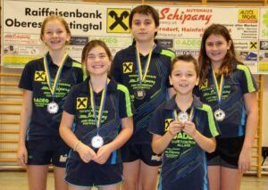 Fünf junge Athleten in blauen und gelben Sportuniformen stehen nebeneinander und posieren für ein Foto. Sie halten ihre Medaillen in den Händen. Hinter ihnen ist ein Banner mit den Worten Raiffeisenbank und Autohaus Schipany.