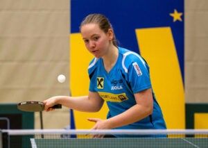 Eine Frau spielt Tischtennis, hält einen Schläger und bereitet sich darauf vor, einen weißen Ball zu schlagen.