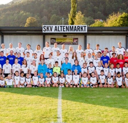 Eine Fußballmannschaft posiert für ein Gruppenfoto auf einem Feld mit einem Hintergrund eines Banners, das 'SKV Altenmarkt' liest.