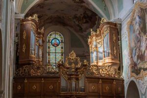 Innenansicht einer Kirche mit einer aufwendigen Holzorgel und einem farbenfrohen Buntglasfenster.