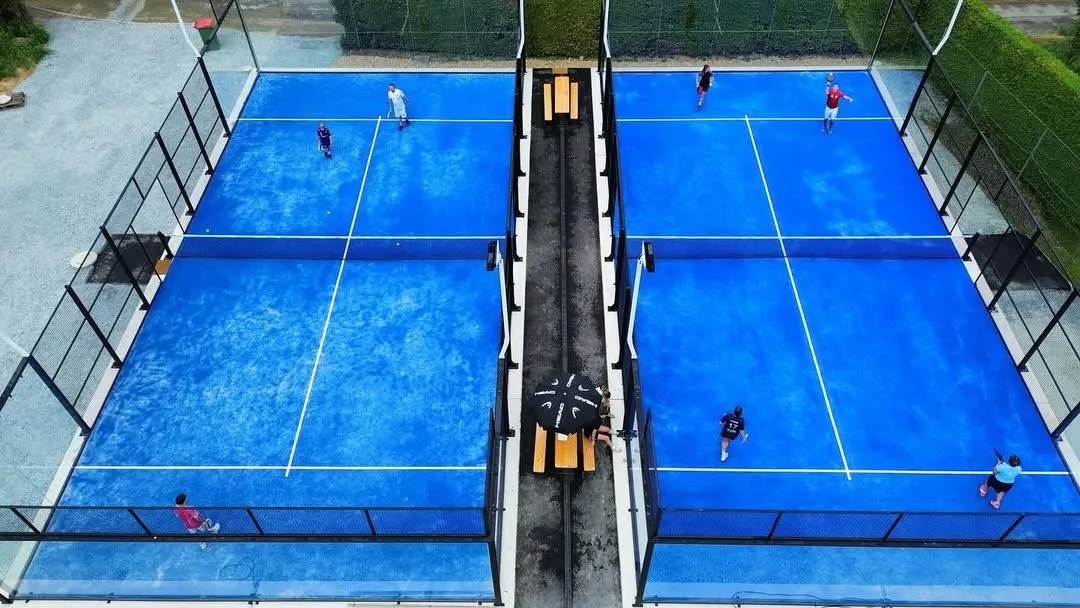 Eine Draufsicht auf einen Tennisplatz mit spielenden Personen. Es gibt vier Spieler, zwei auf jeder Seite. Der Platz hat blauen Boden und weiße Markierungen.