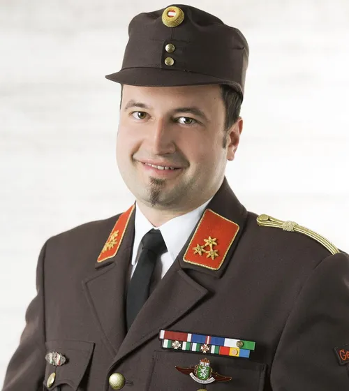 Ein Mann in Uniform mit lächelndem Gesicht steht und posiert für das Foto. Er hat Medaillen und Abzeichen an seiner Uniform.