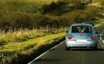 Ein silbernes Auto fährt auf einer Straße mit grünem Gras auf beiden Seiten.