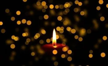 Eine einzelne rote Kerze ist im Dunkeln entzündet, mit Bokeh-Lichtern im Hintergrund, die ein warmes und behagliches Leuchten erzeugen.