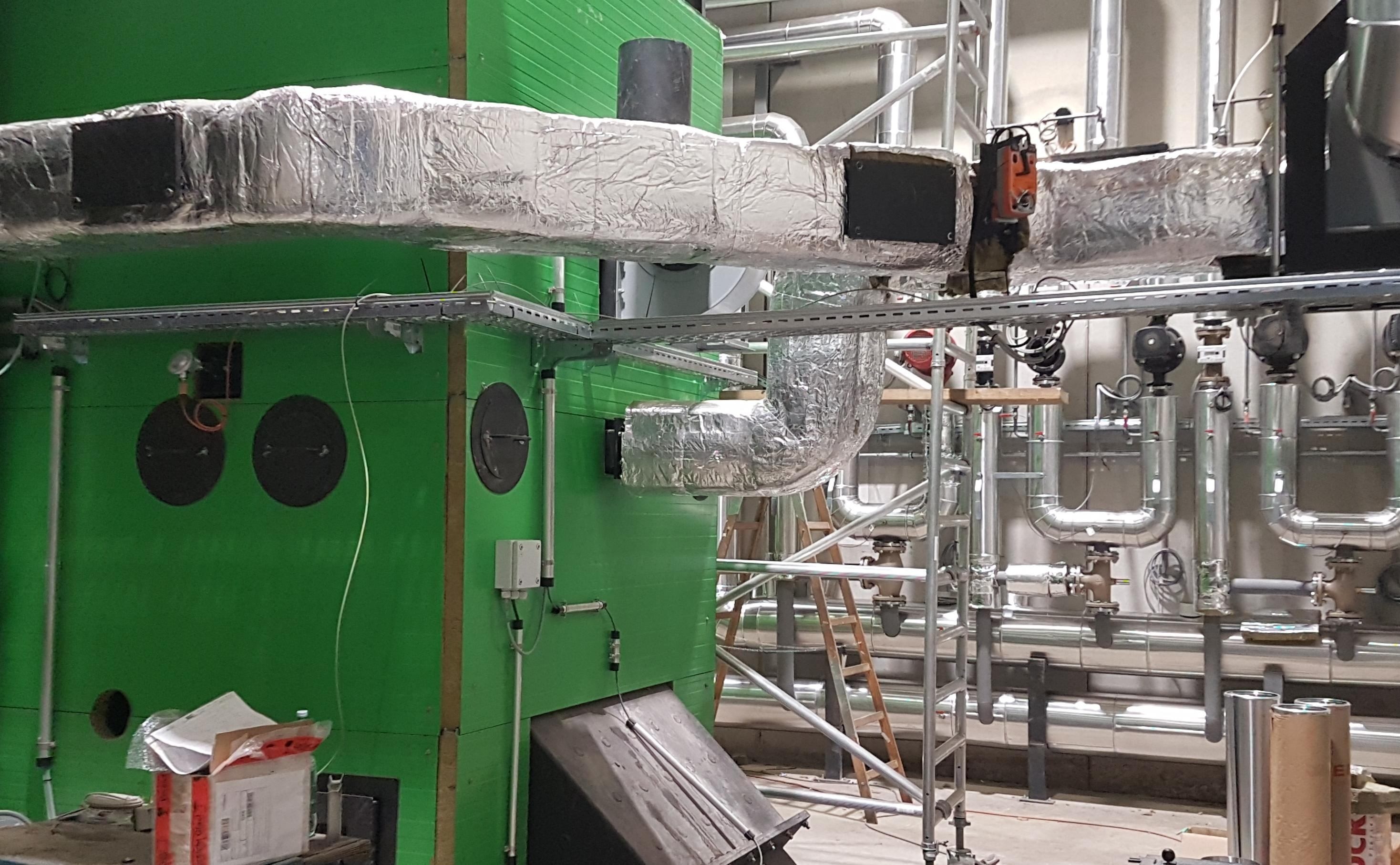 Ein Innenraumbild einer grünen Struktur mit einem angeschlossenen metallischen Rohrsystem. Ein großer Metallrohr ist in Aluminiumfolie eingewickelt.