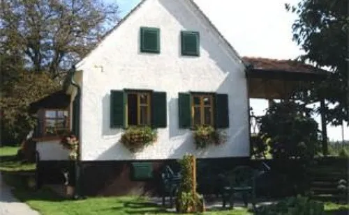 Ein weißes Haus mit grünen Fensterläden und zwei Blumenkästen unter den Fenstern. Davor stehen Gartenstühle und eine Pflanze.