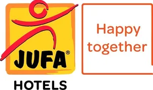 Das Bild zeigt das Logo der JUFA Hotels. Es besteht aus einem gelben Quadrat mit einem roten Symbol und dem Text JUFA Hotels.