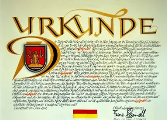 Ein Zertifikat ist auf einem pergamentartigen Hintergrund mit dekorativen Elementen dargestellt. Der Text ist in Deutsch und zeigt goldene und rote Akzente. Das zentrale Bild ist ein Wappenschild mit einer Person, die einen Stab hält. Das Zertifikat enthält verschiedene Daten und erwähnt die Stadt Immenstadt.