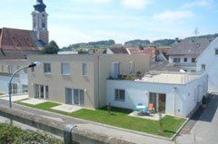 Ein modernes Mehrfamilienhaus mit Rasenfläche vor dem Haus, einer Straßenlampe und einem Turm im Hintergrund.