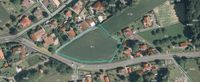 Eine Luftaufnahme eines ländlichen Gebiets mit einem Feld und mehreren Häusern. Das Feld ist mit einer grünen Linie markiert, und die Häuser befinden sich auf beiden Seiten des Feldes. Es gibt eine Straße, die zum Feld führt.
