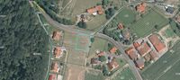 Luftaufnahme eines ländlichen Gebiets mit mehreren Häusern, einer Straße und grünen Feldern. Das zentrale Grundstück ist blau hervorgehoben.