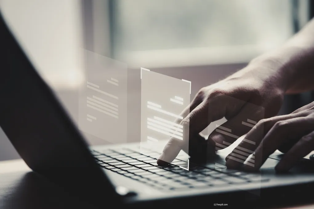 Abschnittsbild: Eine Hand tippt auf einem Laptop, dessen Bildschirm ein Dokument zeigt. Der Hintergrund ist unscharf, was die Konzentration auf die Tippaktion betont.
