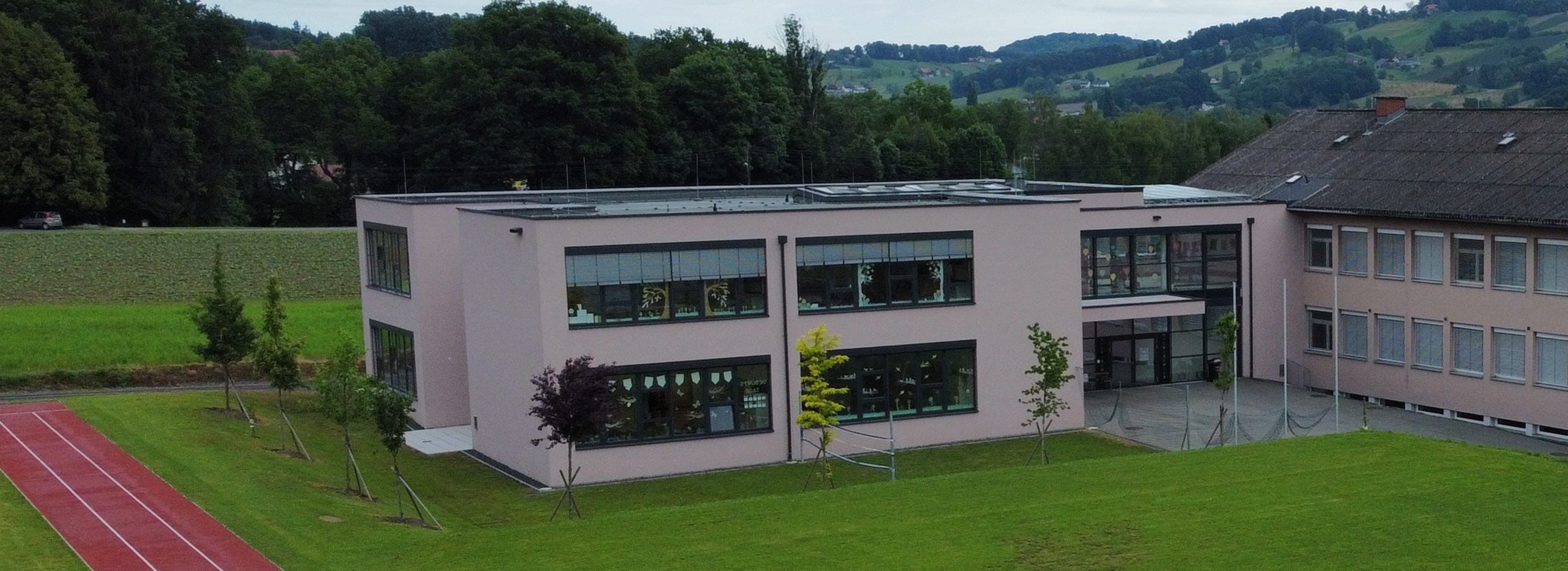 Ein Schulgebäude mit Fenstern, Solarpanelen auf dem Dach und einem gepflegten Rasen davor.