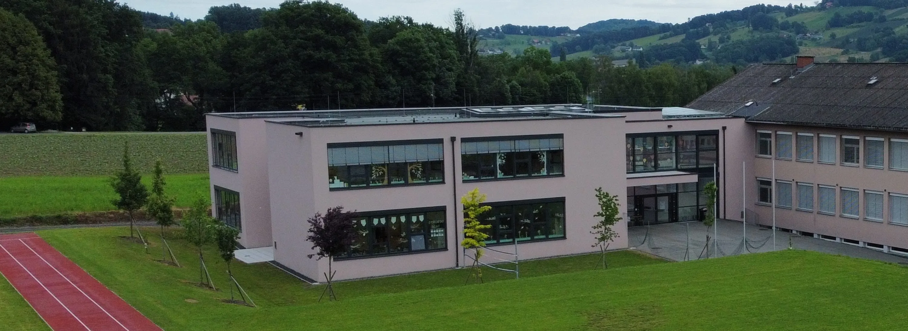 Ein Schulgebäude mit Fenstern, Solarpanelen auf dem Dach und einem gepflegten Rasen davor.