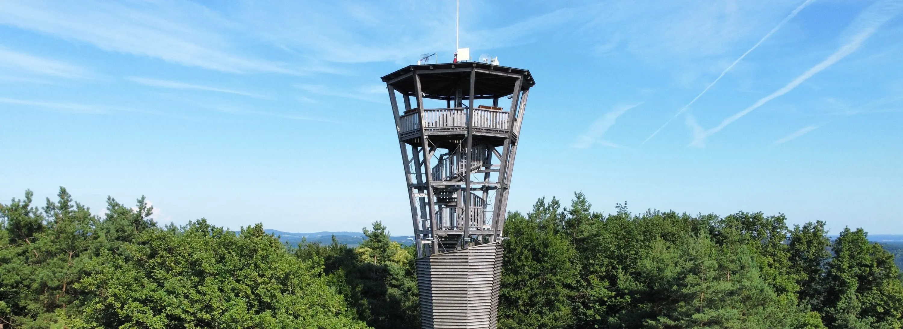 Ein hoher Turm mit einer Wendeltreppe, umgeben von Bäumen, an einem sonnigen Tag