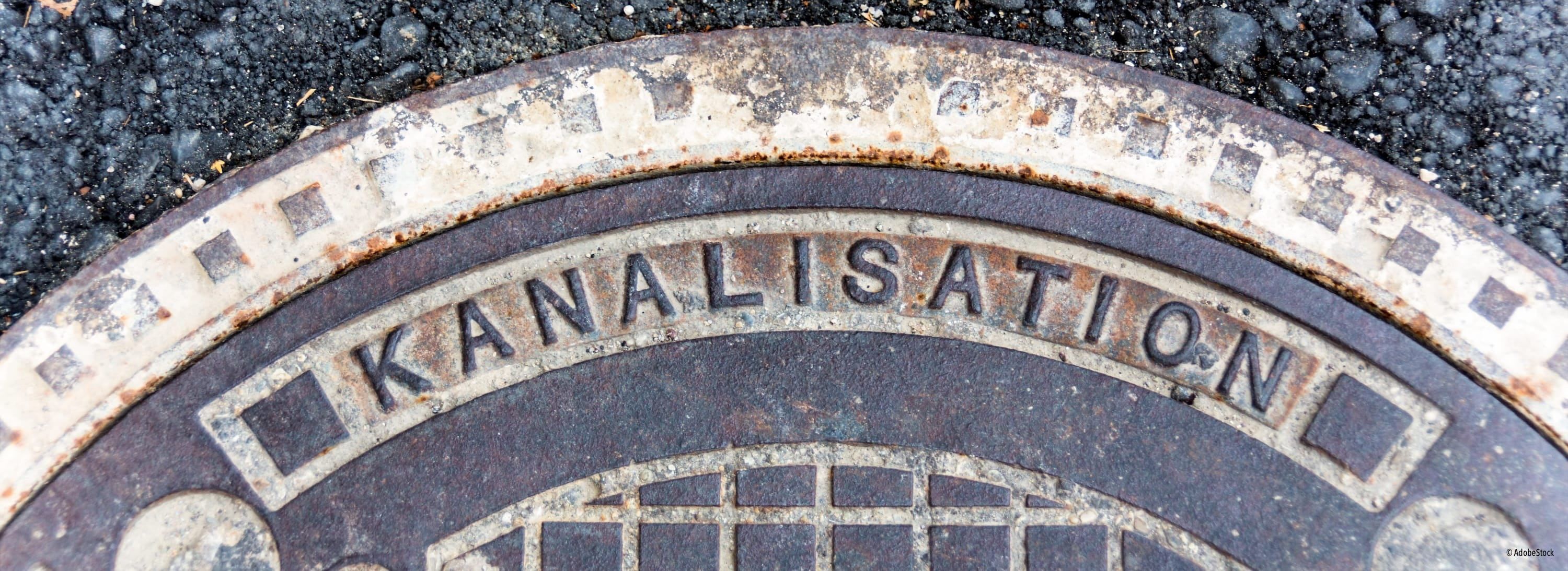 Ein Nahaufnahme einer alten, rostigen Metall-Mannlochabdeckung mit dem Wort 'Analisa' in großen Buchstaben. Die Abdeckung sieht verwittert und gealtert aus und zeigt Anzeichen von Rost und Abnutzung.