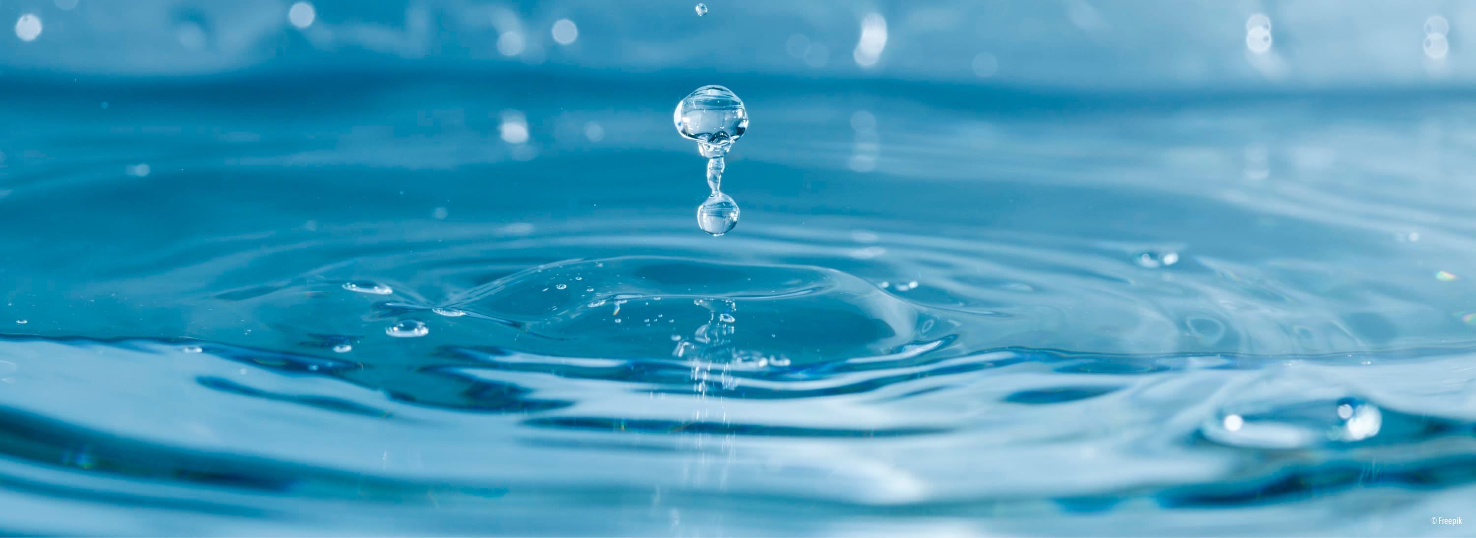 Ein Wassertropfen fällt in einen klaren blauen Pool und erzeugt Wellen. Das Wasser ist rein, mit kleinen Blasen sichtbar.