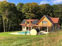 Ein modernes Haus mit Solarpanelen auf dem Dach, umgeben von einem üppigen grünen Rasen und Bäumen. Es hat einen Swimmingpool und Gartenmöbel.