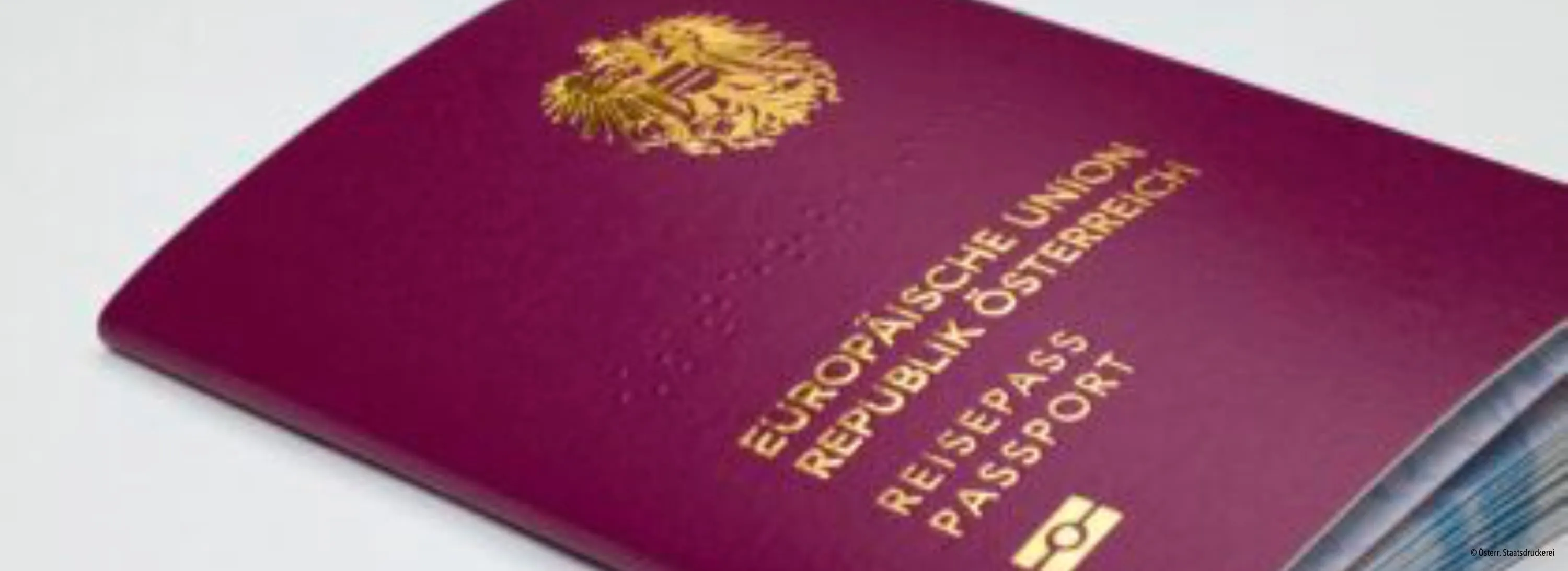 Eine Nahaufnahme eines österreichischen Reisepasses mit goldenen Emblemen und Text in Gold und Schwarz auf einem burgunderroten Cover.