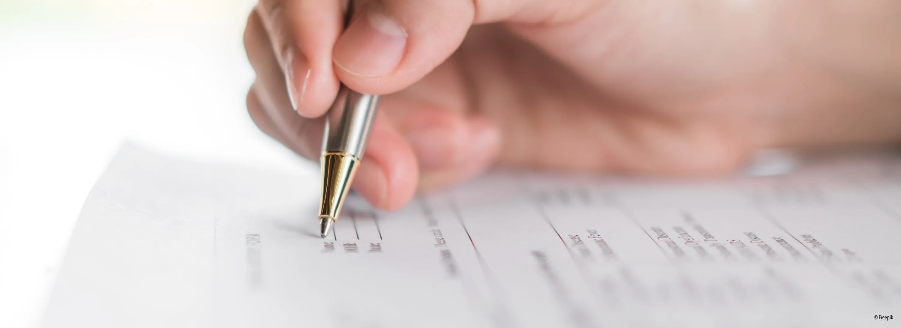 Eine Nahaufnahme der Hand einer Person, die einen Stift hält und auf einem Formular mit verschwommenem Text und Feldern schreibt.