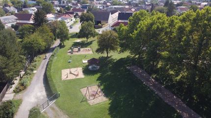 Ein Luftbild eines Parks mit einem Spielplatz, einer Schaukel und einem Pavillon, umgeben von Bäumen und Gras.