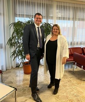 Ein Mann und eine Frau stehen in einem Raum mit einem Topf und roten Stühlen.