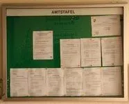Ein Bulletinbrett mit grünem Hintergrund, beschriftet mit 'AMTSTAFEL'. Es sind mehrere weiße Blätter mit gedrucktem Text befestigt, in einem Rastermuster angeordnet. Die Blätter scheinen Jobangebote oder Ankündigungen zu enthalten.