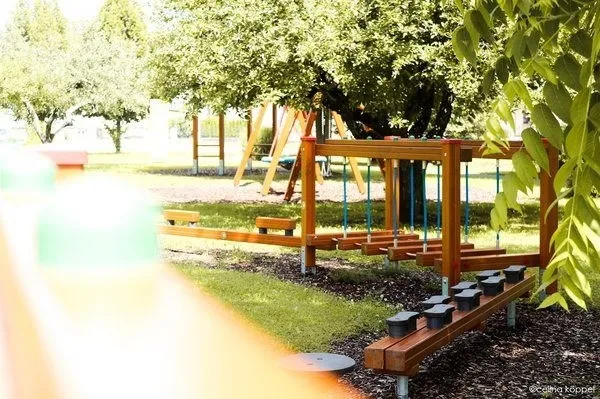 Ein Spielplatz mit Holzstrukturen und einer Schaukel unter Bäumen in einem Park.