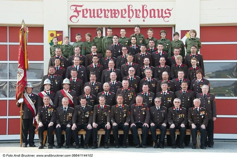 Eine Gruppe von Feuerwehrleuten, in Uniform gekleidet, posiert für ein Foto vor einem Feuerwehrhaus.