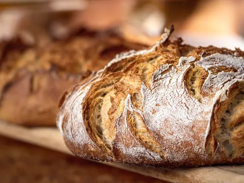 Ein Nahaufnahme eines frisch gebackenen Laibs rustikales Brot, bestreut mit Mehl, auf einem Holzbrett.