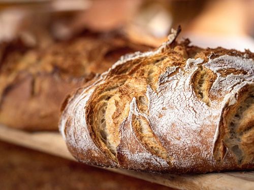 Ein Nahaufnahme eines frisch gebackenen Laibs rustikales Brot, bestreut mit Mehl, auf einem Holzbrett.
