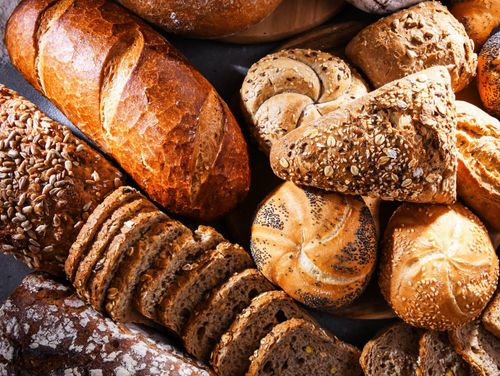 Verschiedene Brotsorten, darunter Vollkorn-, Roggen- und Sauerteigbrot, sind auf einer dunklen Oberfläche ausgestellt. Einige sind geschnitten, andere ganz.