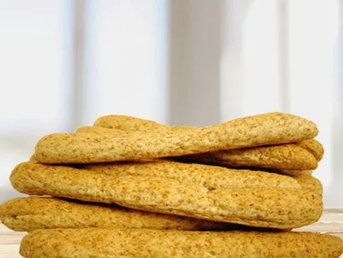 Ein Stapel goldener Brötchen, möglicherweise Pitabrot, ruht auf einer Holzoberfläche. Der Hintergrund ist weiß, und das Licht reflektiert sich auf dem Brot.