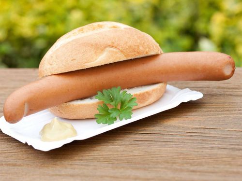 Ein Hot-Dog-Sandwich mit Senf und Petersilie auf einem weißen Teller auf einem Holztisch.
